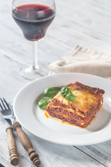 Portion of lasagne with a glass of wine on the wooden table