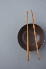 Dark Empty Bowl with Brown Bamboo Chopsticks on Grey Background. Japanese Chinese Asian Cuisine. Menu Poster Template. Copy Space