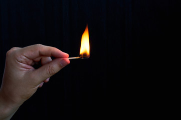 Hand holding burning match stick on black background