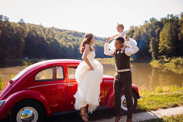 Mom and dad jump with their little daughter before a red car