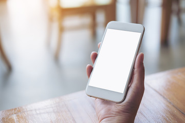 Mockup image of hand holding white mobile phone with blank screen on table in cafe