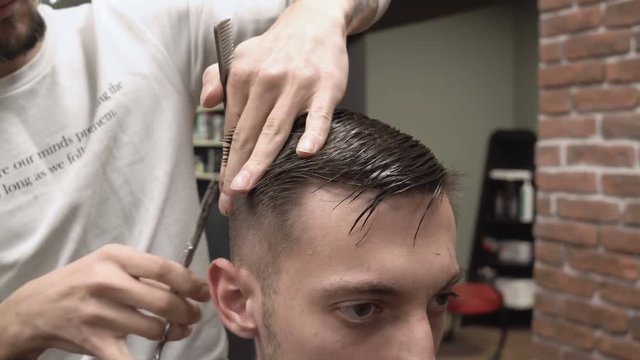 Young male hairdresser cuts a young hipster guy with scissors close-up 4k.