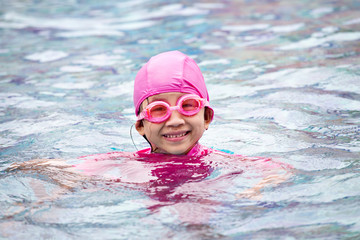 Smiling baby girl wearing swimming glasses in swimming pool.