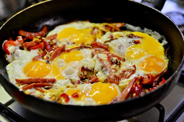Shakshuka - fried eggs with tomatoes, onion, pepper and spices in iron pan, dark style