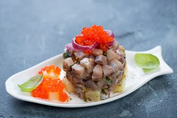 Herring tartare with red caviar topping and potato bedding served on a fish-shaped plate, selective focus