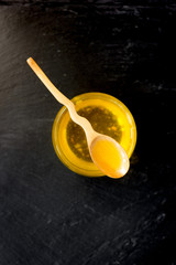 Fresh ghee butter in a wooden spoon over black stone background.