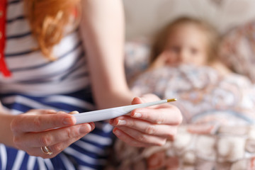 Obraz na płótnie Canvas How to treat a child from a cold to bring down the temperature Close up of a mother's hand with a thermometer.