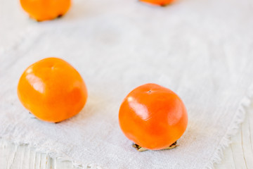 Group of ripe persimmons on white fabric material.
