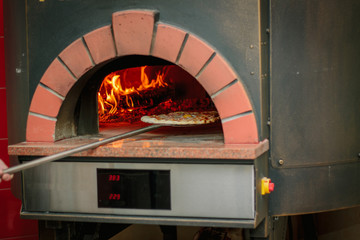 Pizza on shovel in a traditional pizza oven.