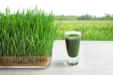 Glass of juice and wheat grass field  on background