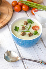 Beautiful asparagus cream soup with toasted bread on white wooden table.
