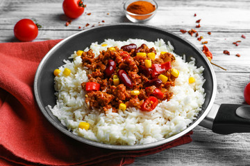 Frying pan with chili con carne and rice on table