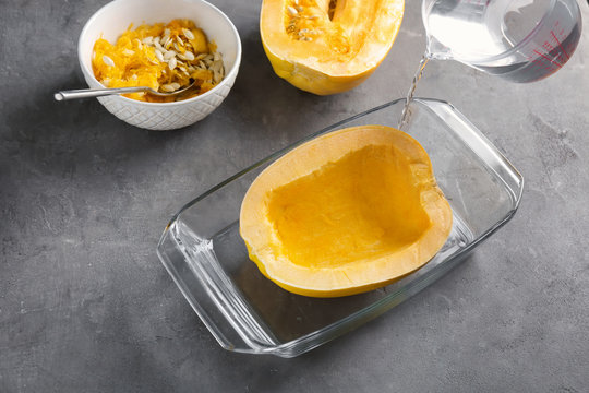 Pouring water into baking dish with cut spaghetti squash on table