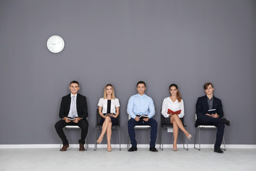 Group of people waiting for job interview on gray wall background