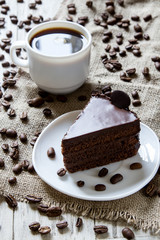 Cup of espresso, coffee beans on table with sackcloth, piece of chocolate cake