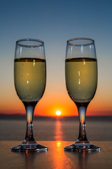 Couple of glasses of wine at sunset on the table, closeup, sun between glasses