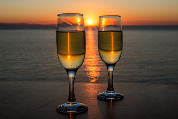 Romantic evening, sunset, two wineglasses, sun path on the water between two wineglasses with wine