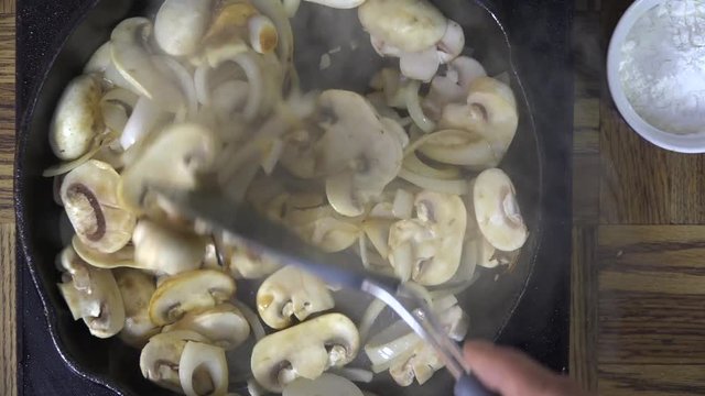Stirring mushrooms and onions in a cast iron skillet
