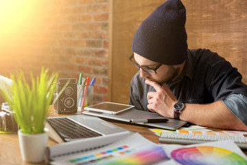 Young creative artist of web design in hat with graphic tablet in modern loft office