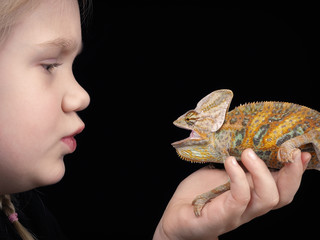 Chameleon on the hand of a small child. The dark background