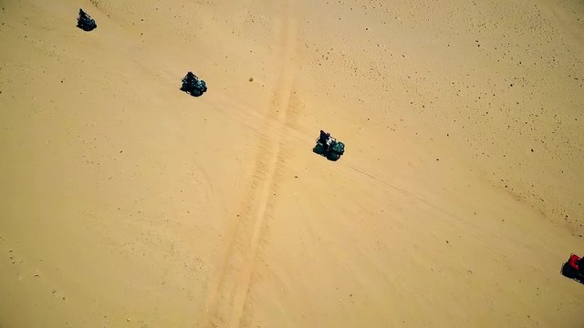 Skyline Aerial view of young men riding quad bikes over sand dunes in desert. The race in difficult conditions on the sand on a quad bike.