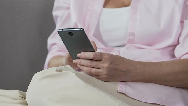 Retired female holding smartphone scrolling its screen, easy mobile applications