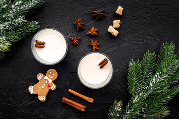 Merry christmas in winter evening with alcohol drink. Eggnog with gingerbread cookie, cinnamon and spruce on black desk background top view