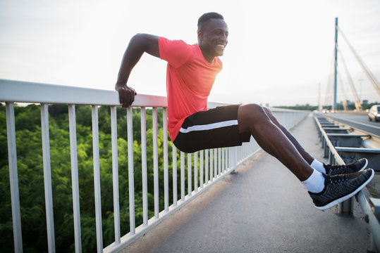Attractive afro-american man stretching on the bridge between fences in the morning.