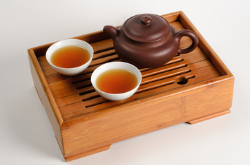 Teapot and two cups of tea on a wooden stend on white background