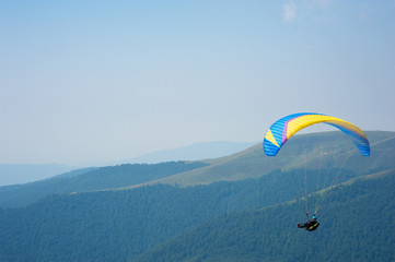 A paraglider flies over a mountain valley on a sunny summer day. Paragliding in the Carpathians in...