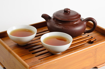 Teapot and two cups of tea on a wooden stend on white background