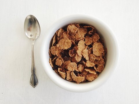 A bowl of fresh breakfast cereal on a white table with a silver spoon