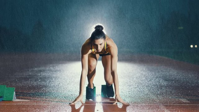  Female athlete training at running track in the dark & in the rain. Slowmo