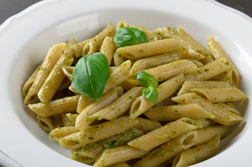 Whole wheat Pasta with homemade pesto sauce in a white plate on a dark stone slate background, closeup