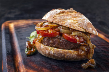 Barbecue Wagyu Hamburger with onions and tomatoes as close-up on a burnt cutting board