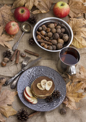 A composition of nuts, pancakes, bananas and apple on a nice autumn themed background