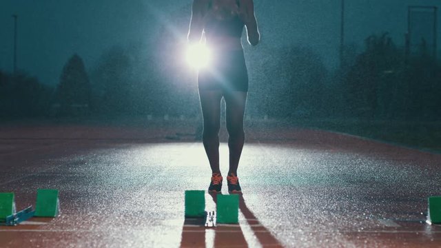  Female athlete training at running track in the dark & in the rain. Slowmo