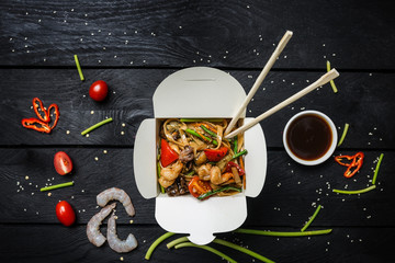 Udon stir fry noodles with seafood in a box on black background. With chopsticks and sauce. - obrazy, fototapety, plakaty