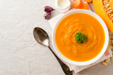 Pumpkin and carrot cream soup with parsley on gray stone background.