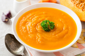 Pumpkin and carrot cream soup with parsley on gray stone background.