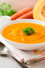 Pumpkin and carrot cream soup with parsley on gray stone background.