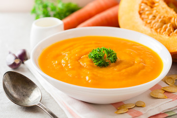 Pumpkin and carrot cream soup with parsley on gray stone background.