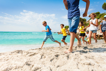 Group of happy kids running on white sand beach