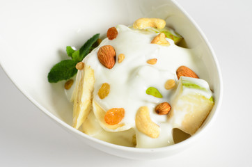 Fruit salad with yogurt and nuts in a bowl on white background