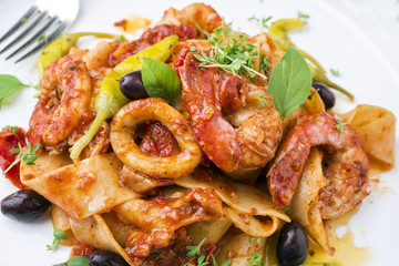 Italian tagliatelle con gamberi e calamari in salsa di pomodoro with olives and peperoni as close-up on a plate