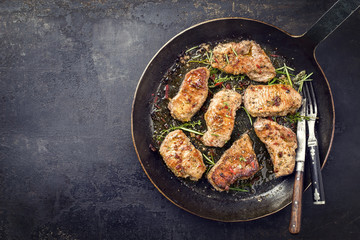 Fried saddle of pork steak with herb as top view in a frying pan with copy space left