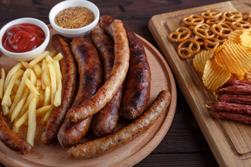 Oktoberfest food, appetizing beer snacks set for big company. Grilled sausages, salami, chips, pretzel crackers and french fries served with spicy tomato sauce and mustard, close up