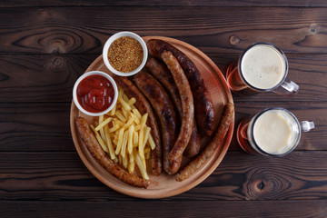 Appetizing beer snacks plate. Top view on table with grilled sausages and french fries served with spicy tomato sauce, mustard and dark beer. Oktoberfest food, pub concept
