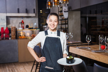 young girl with a beautiful smile a waiter holds in her hands an order sweet dessert dish of Italian cuisine. Dressed in a crusty apron and a white shirt