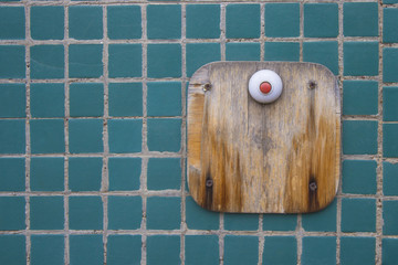 Red button on wood plate on tile wall